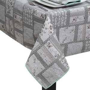 May include: A grey and white patchwork tablecloth with a light blue border. The tablecloth has a floral pattern and is made of a soft, quilted fabric.
