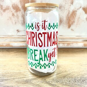 May include: A clear glass jar with a bamboo lid and a red and green Christmas themed design that says "is it Christmas break yet?"