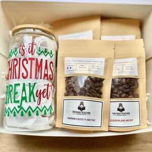 May include: A gift box filled with three bags of coffee beans and a glass jar with a Christmas-themed design that says "Is it Christmas break yet?" The coffee bags are labeled with the text "The Bad Teacher Company" and the text "Surprise Faculty Meeting" and "Lesson Plans Are Due".