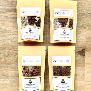 May include: Four small bags of coffee beans with labels that say "The Bad Teacher Company". The bags are labeled with different coffee blends and roast levels. The blends are "Lesson Plans Are Due", "Classroom Walkthrough", "Surprise Faculty Meeting", and "Maestra Blend".