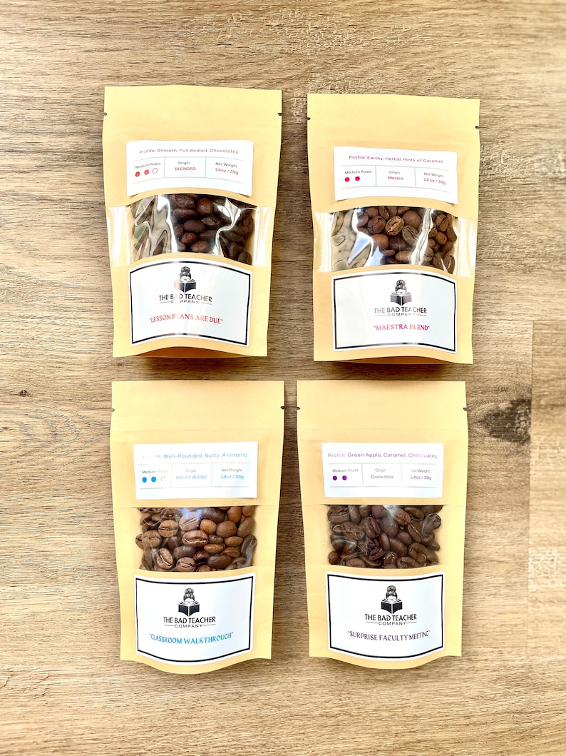 May include: Four small bags of coffee beans with labels that say "The Bad Teacher Company". The bags are labeled with different coffee blends and roast levels. The blends are "Lesson Plans Are Due", "Classroom Walkthrough", "Surprise Faculty Meeting", and "Maestra Blend".