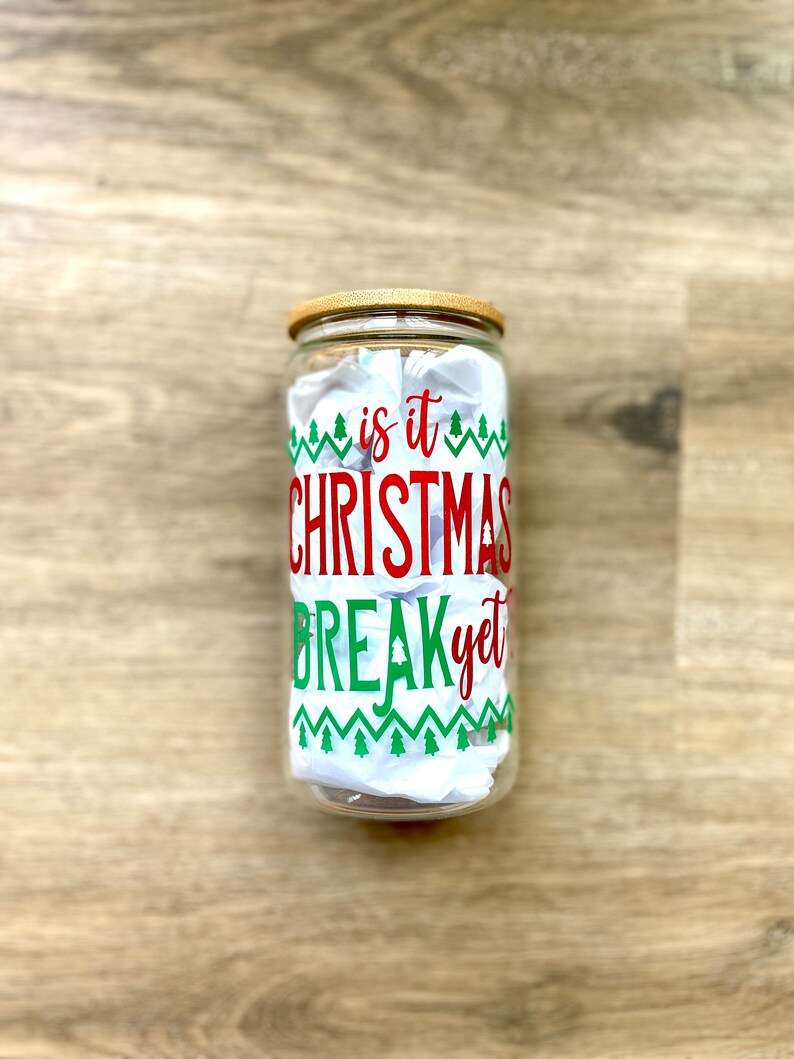 May include: A clear glass jar with a wooden lid and a red and green design that says "is it Christmas break yet".