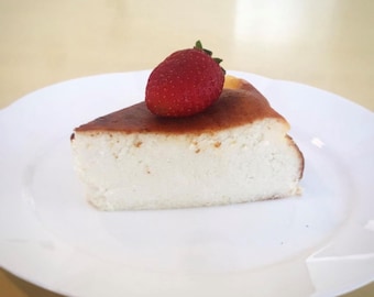 May include: A slice of cheesecake topped with a fresh strawberry on a white plate.