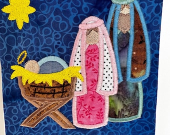 May include: A blue fabric panel with an embroidered nativity scene. The scene includes a manger with a baby, Mary, and Joseph. A yellow star is above the manger.