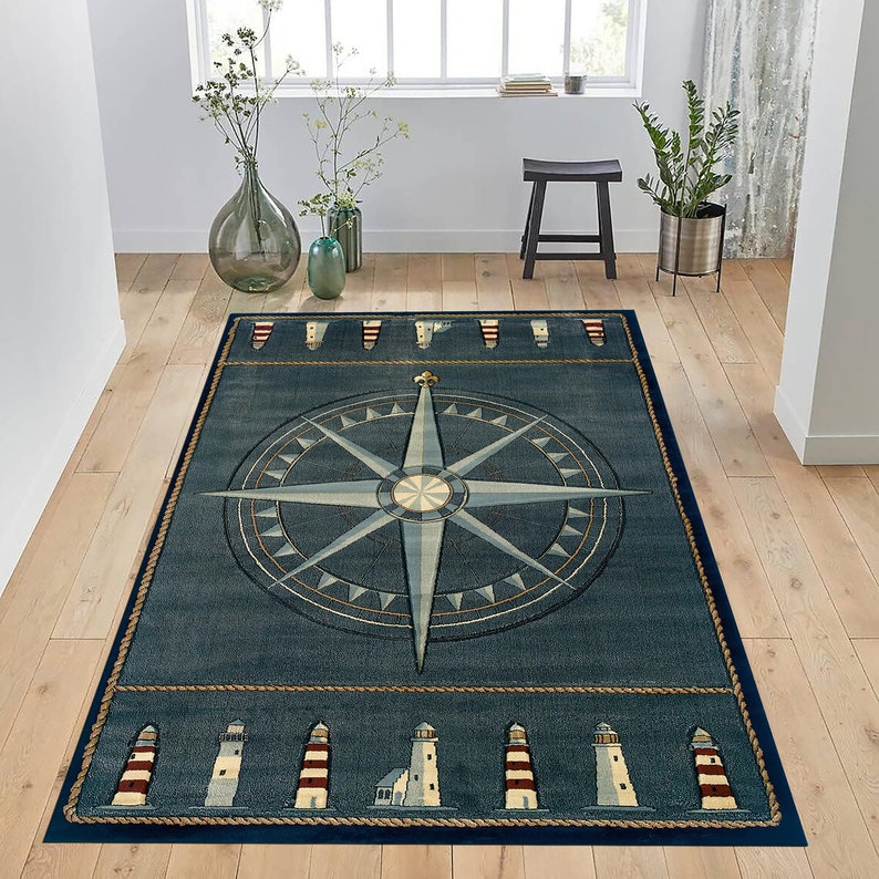 Pu&ograve; includere: Tappeto rettangolare blu navy a tema nautico. Presenta un grande disegno di rosa dei venti nei toni del blu e beige. Il bordo include illustrazioni di fari e dettagli di corda, creando un'estetica costiera.