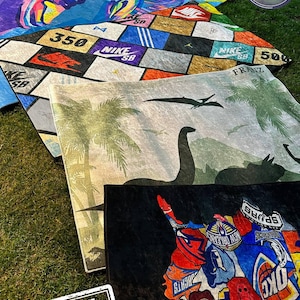 Pu&ograve; includere: Una collezione di tappeti colorati con vari disegni, tra cui una grafica di scarpe, un design "350" e una scena di dinosauri. I tappeti sono esposti sull'erba, con un timbro "SAMPLE" nell'angolo. I tappeti sono di "Creative Rug Design".