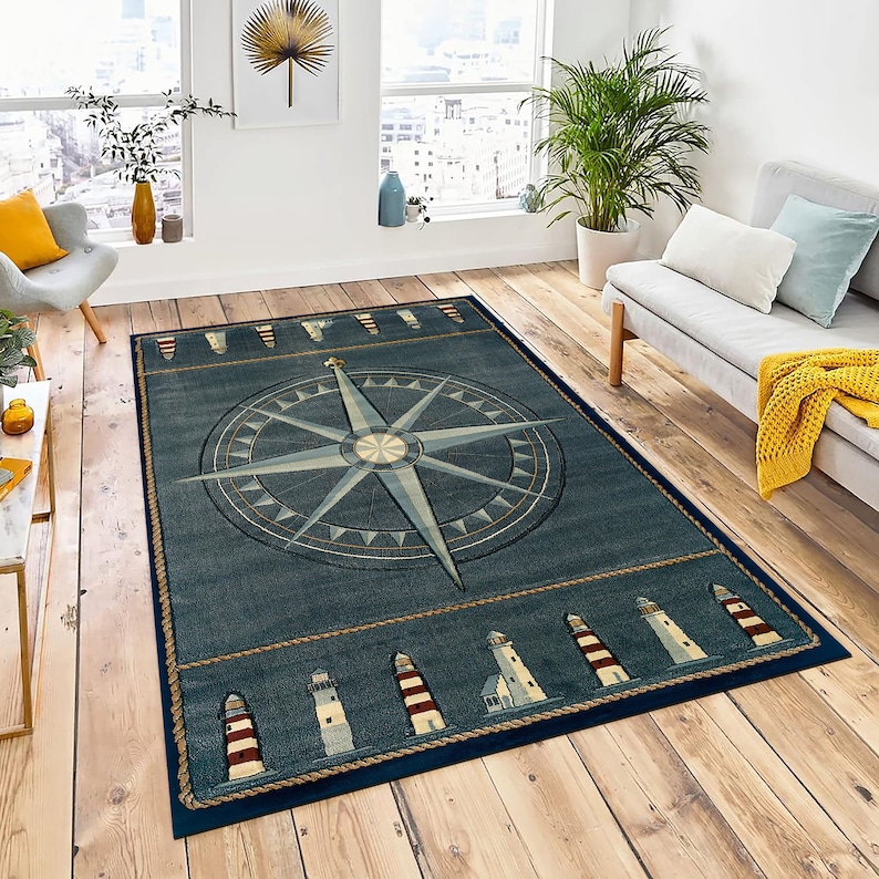 Pu&ograve; includere: Un tappeto rettangolare blu navy a tema nautico. Presenta un grande disegno di rosa dei venti nei toni del blu e beige. Il bordo include un motivo a corda e immagini di fari con strisce rosse e bianche. Il tappeto &egrave; posto su un pavimento in legno.