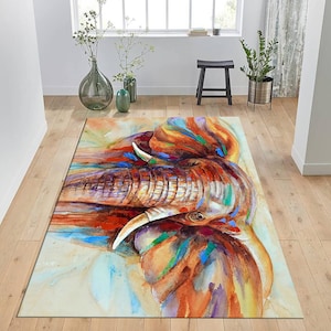 May include: A watercolor painting of an elephant's head with colorful splashes of paint. The elephant's trunk is raised and its eyes are closed. The background is a light beige color.