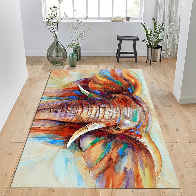 May include: A watercolor painting of an elephant's head with colorful splashes of paint. The elephant's trunk is raised and its eyes are closed. The background is a light beige color.