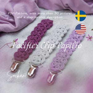 May include: Three crocheted pacifier clips in purple, gray, and white with silver clips. The clips are labeled "Pacifier Clip Papilio".