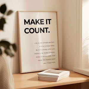 May include: A framed print with the words "MAKE IT COUNT" in bold black letters. Below, smaller text reads "Life is not always perfect..." The print is on a desk with a stack of books. The overall theme is motivational.