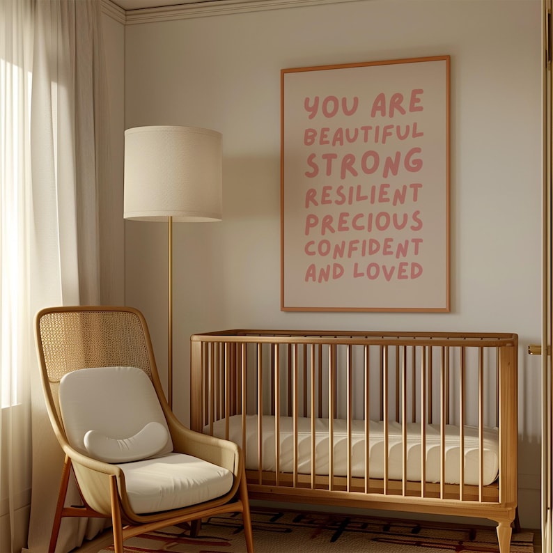 May include: A nursery room featuring a cot, a wicker chair, and a framed print with the text "You are beautiful strong resilient precious confident and loved" in pink lettering on a white background.