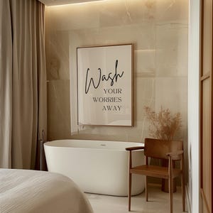 May include: A white bathtub with a framed print above it that reads "Wash your worries away". A wooden chair is to the right of the tub.