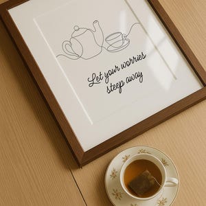 Puede incluir: Una impresión enmarcada con un dibujo lineal de una tetera y una taza, con las palabras "Let your worries steep away". Una taza de té con té y una bolsita de té se encuentra en un platillo floral sobre una mesa de madera.