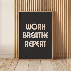 May include: A black framed poster with white text that reads "WORK  BREATHE  REPEAT" against a wood slat background.