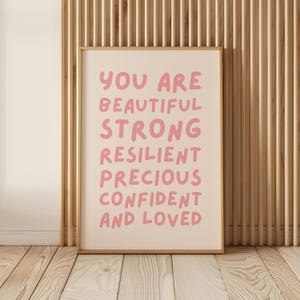 May include: A framed print with the text "You are beautiful strong resilient precious confident and loved" in pink lettering on a cream background.