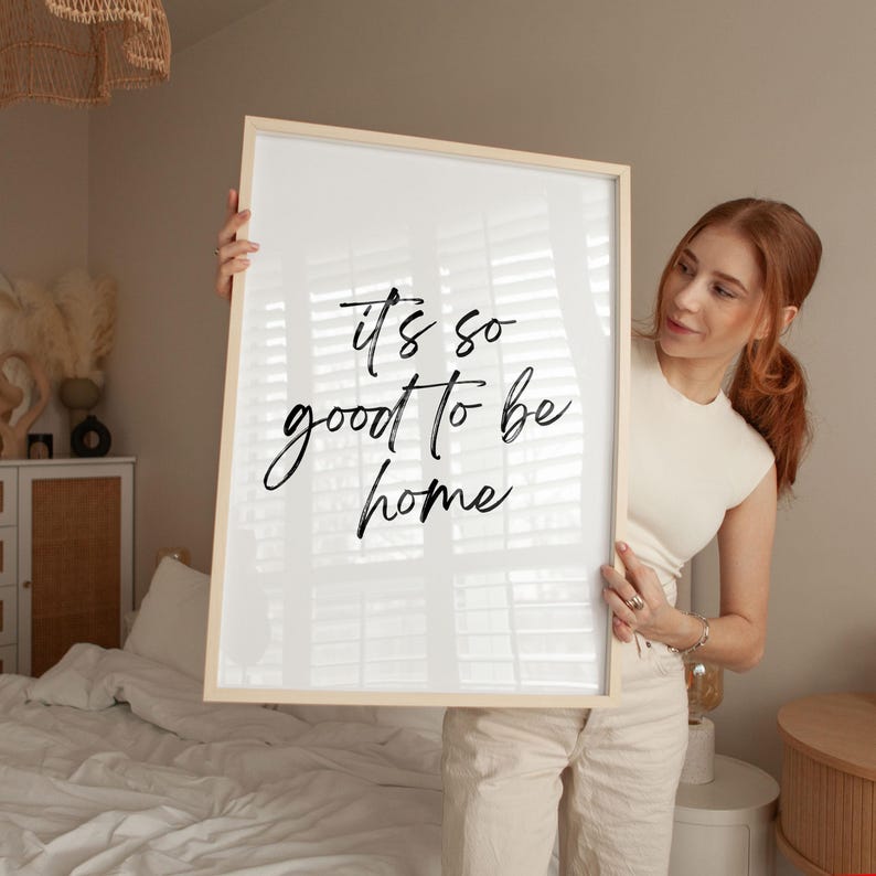 May include: A white framed print with black calligraphy that reads "It's so good to be home".