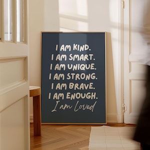 Może przedstawiać: Oprawiony wydruk z ciemnoniebieskim tłem i białym tekstem. Tekst brzmi: „I AM KIND. I AM SMART. I AM UNIQUE. I AM STRONG. I AM BRAVE. I AM ENOUGH. I am Loved.” Rama jest w kolorze jasnobrązowym.