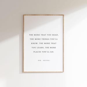 以下が含まれることがあります： 白い背景に黒い文字が書かれた額入りのプリント。テキストは次のとおりです。「読めば読むほど、知ることは増える。学べば学ぶほど、行ける場所は増える。」 - DR. SEUSS.