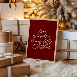 May include: A framed red sign with the text "Have yourself a Merry little Christmas" in white script. The sign is in front of a Christmas tree and wrapped gifts.