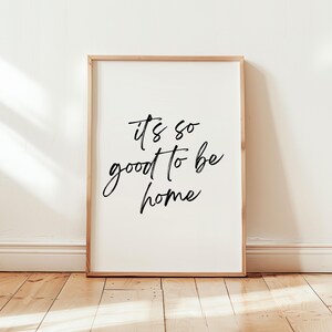 May include: A white framed print with black calligraphy that reads "it's so good to be home".