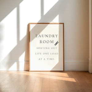 May include: A framed print with the text "Laundry Room Sorting Out Life One Load At A Time."  A small illustration of a clothespin is next to the word "Room."