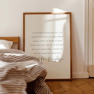 May include: A framed print with a light background and brown frame. The print features a romantic quote in black script. The text reads, "So it's not gonna be easy... I want all of you, forever, every day." The print is displayed in a bedroom setting.