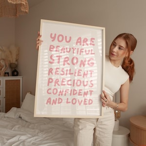 May include: A white framed print with the text "You are beautiful strong resilient precious confident and loved" in pink lettering.