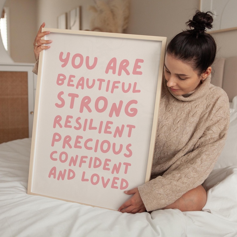 May include: A framed print with the text "You are beautiful strong resilient precious confident and loved" in pink lettering on a white background.