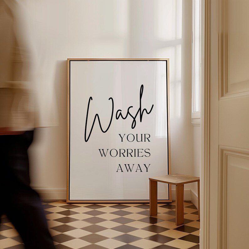 May include: A white framed print with black text that reads "Wash your worries away". The print is hanging on a wall in a bathroom with a checkered floor.