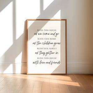 Op de afbeelding: Een ingelijst print met een witte achtergrond en zwarte tekst die luidt: "Zegen dit huis als we komen en gaan. Zegen dit huis als de kinderen opgroeien. Zegen onze familie als ze samenkomen. Zegen dit huis met liefde en vrienden."