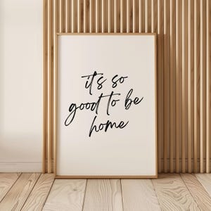 May include: A white framed print with black calligraphy that reads "it's so good to be home".