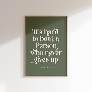 May include: A framed print with a green background and the quote "It's hard to beat a Person who never gives up" in a white, elegant font. The quote is attributed to Babe Ruth.