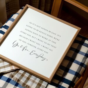 May include: A framed print with a white background and black text. The text includes the phrases "So it's not gonna be easy" and "You & Me... Everyday". The frame is made of light brown wood.