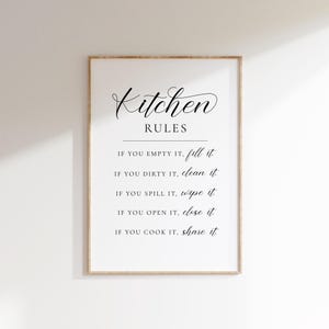 Könnte beinhalten: Ein schwarz-weißes druckbares Schild mit dem Text "Küchenregeln" und einer Liste von Regeln für die Küche: "Wenn du es leerst, fülle es. Wenn du es schmutzig machst, putze es. Wenn du etwas verschüttest, wische es ab. Wenn du es öffnest, schließe es. Wenn du kochst, teile es."