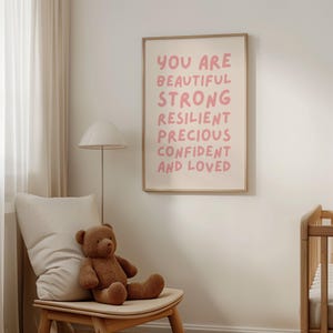 May include: A pink and white framed print with the text "You are beautiful strong resilient precious confident and loved" in a pink font.