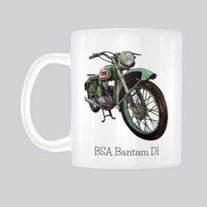 May include: White ceramic mug featuring a watercolor illustration of a vintage green BSA Bantam D1 motorcycle. The mug has a curved handle and the text "BSA Bantam D1" is printed below the motorcycle image.