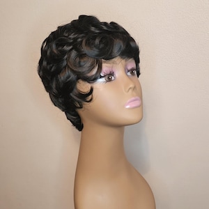 May include: A short, curly black wig with a side part. The wig is styled in a pixie cut with loose curls. The wig is on a mannequin head.