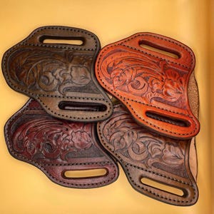 May include: Four leather holsters with intricate floral designs. The holsters are in shades of brown, red, and orange.