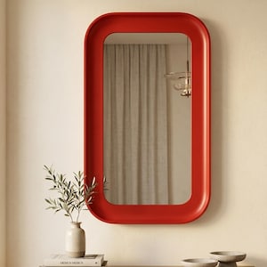 May include: A rectangular wall mirror featuring a bold, solid red frame with rounded corners. The mirror has a smooth, continuous border design that surrounds the reflective glass surface, providing a clean and uniform appearance for wall mounting.