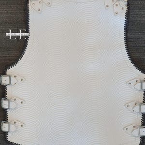 K&ouml;nnte beinhalten: Wei&szlig;e Lederweste mit Schlangenhautstruktur, silbernen Schnallen und Nieten. Die Weste hat eine schwarz gen&auml;hte Paspel und ein einzigartiges Design. Das Leather Escort-Logo ist auf der linken Seite sichtbar.