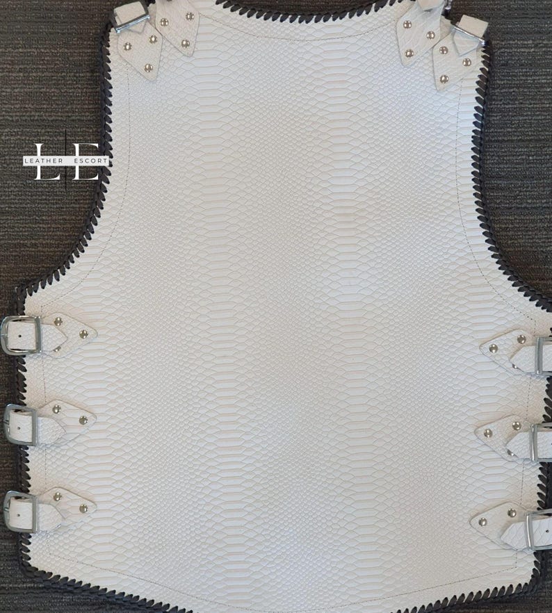 K&ouml;nnte beinhalten: Wei&szlig;e Lederweste mit Schlangenhautstruktur, silbernen Schnallen und Nieten. Die Weste hat eine schwarz gen&auml;hte Paspel und ein einzigartiges Design. Das Leather Escort-Logo ist auf der linken Seite sichtbar.