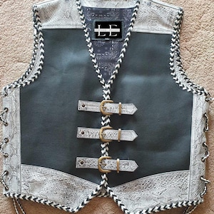 Può includere: Gilet di pelle nera con cuciture bianche e un motivo a pelle di serpente bianca sul davanti e sul retro. Il gilet ha tre fibbie e un'etichetta che dice "LE LEATHER ESCORT".