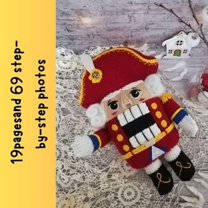 Puede incluir: Un mu&ntilde;eco de cascanueces de crochet con un gorro rojo, barba blanca y un uniforme amarillo y rojo. El mu&ntilde;eco est&aacute; sentado sobre una superficie de crochet blanca.