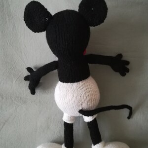 May include: A black and white knitted Mickey Mouse toy with a red nose. The toy is lying on its back with its arms outstretched and its legs bent.