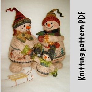 Könnte beinhalten: Strickmuster-PDF für drei gestrickte Schneemänner. Die Schneemänner tragen Mützen, Schals und Fäustlinge. Der kleinste Schneemann hält einen kleinen Schlitten.