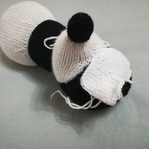 May include: A white and black knitted toy with a black pom-pom on top. The toy is shaped like a bee with a white body and black stripes.