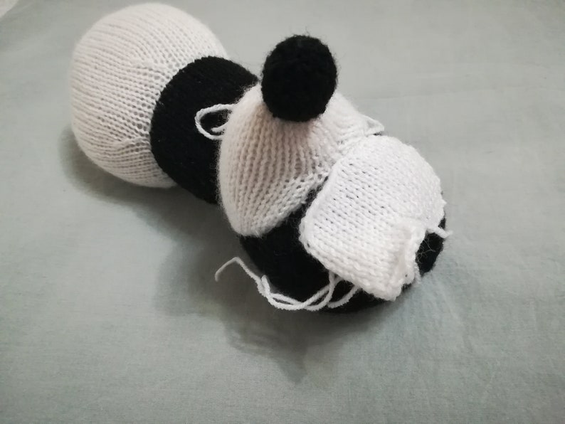 May include: A white and black knitted toy with a black pom-pom on top. The toy is shaped like a bee with a white body and black stripes.