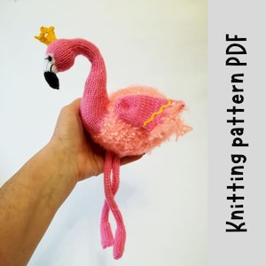 May include: A knitted pink flamingo toy wearing a yellow crown. The flamingo has a black beak, white eyelashes, and fluffy pink feathers. The image includes the text "Knitting pattern PDF" on the right side.