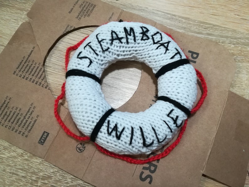 May include: White knitted life preserver with black and red trim. The words "STEAMBOAT WILLIE" are embroidered on the front.